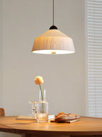 Above a round table with a flower in a glass and bread rolls, this Clérachic pendant's beige shade glows warm.