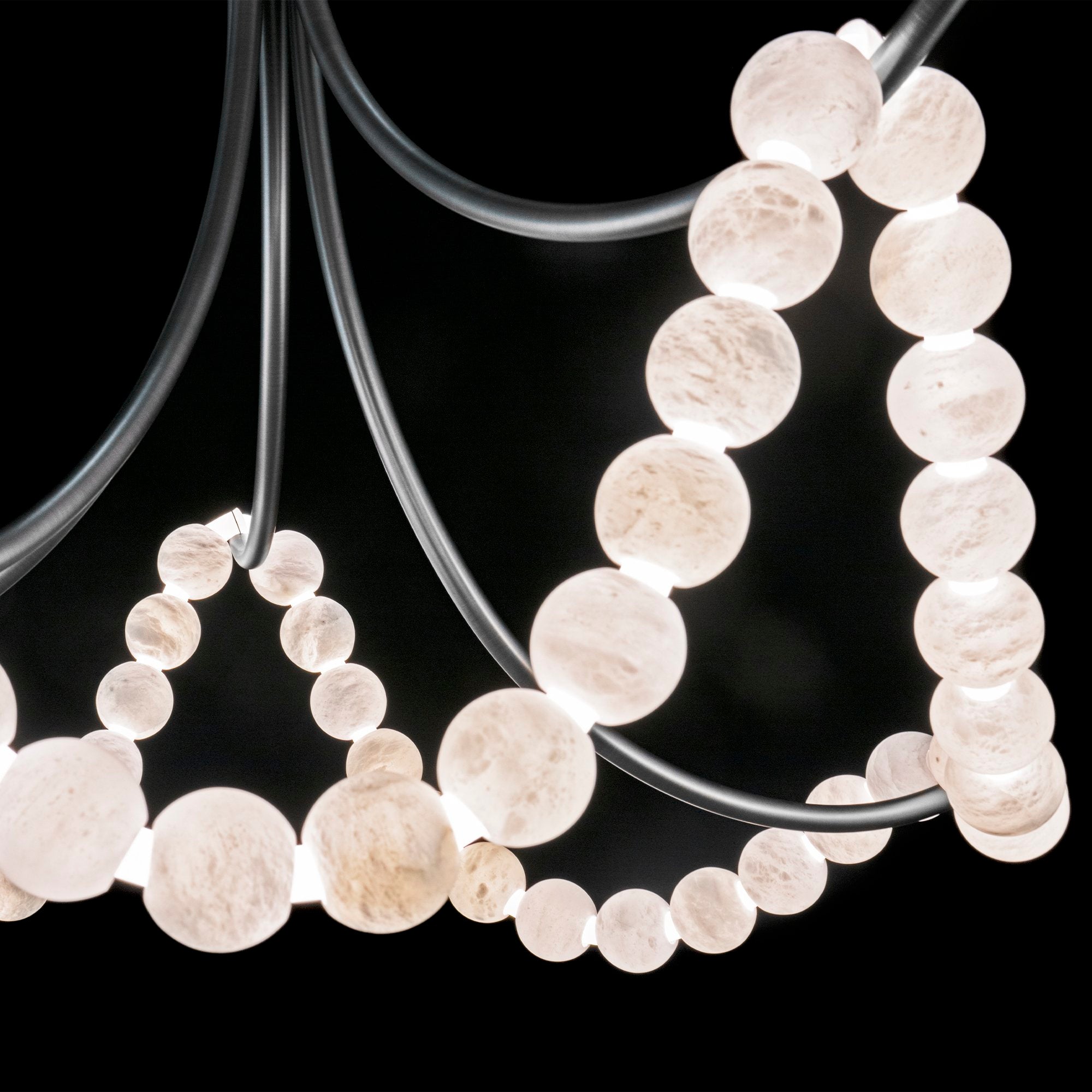 Close-up of the nickel version, lit alabaster beads strung along dark curved arms against black