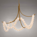 Parel alabaster chandelier in gold, lit, its bead strands draped between four curved brass arms
