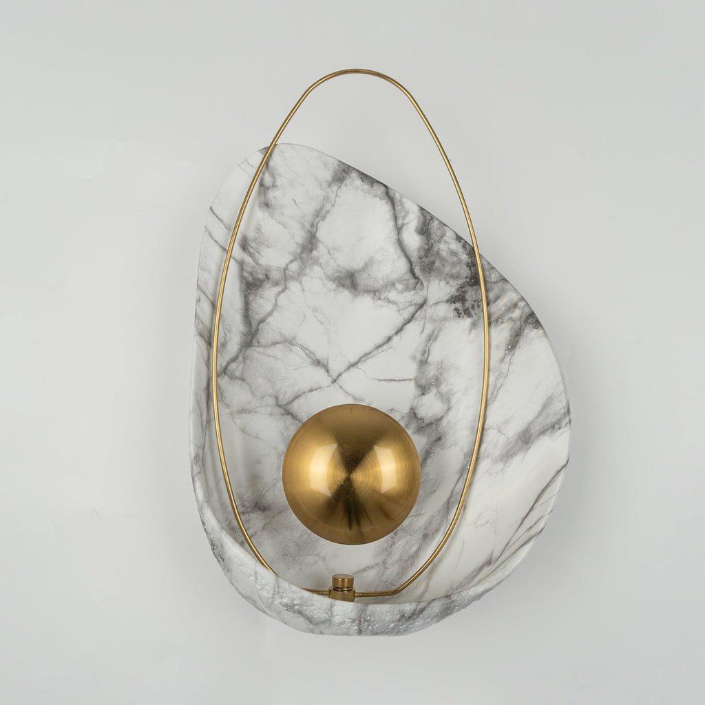 Unlit sconce straight on against a white wall, the matte brass orb centred on the marbled shell.
