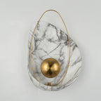 Unlit sconce straight on against a white wall, the matte brass orb centred on the marbled shell.