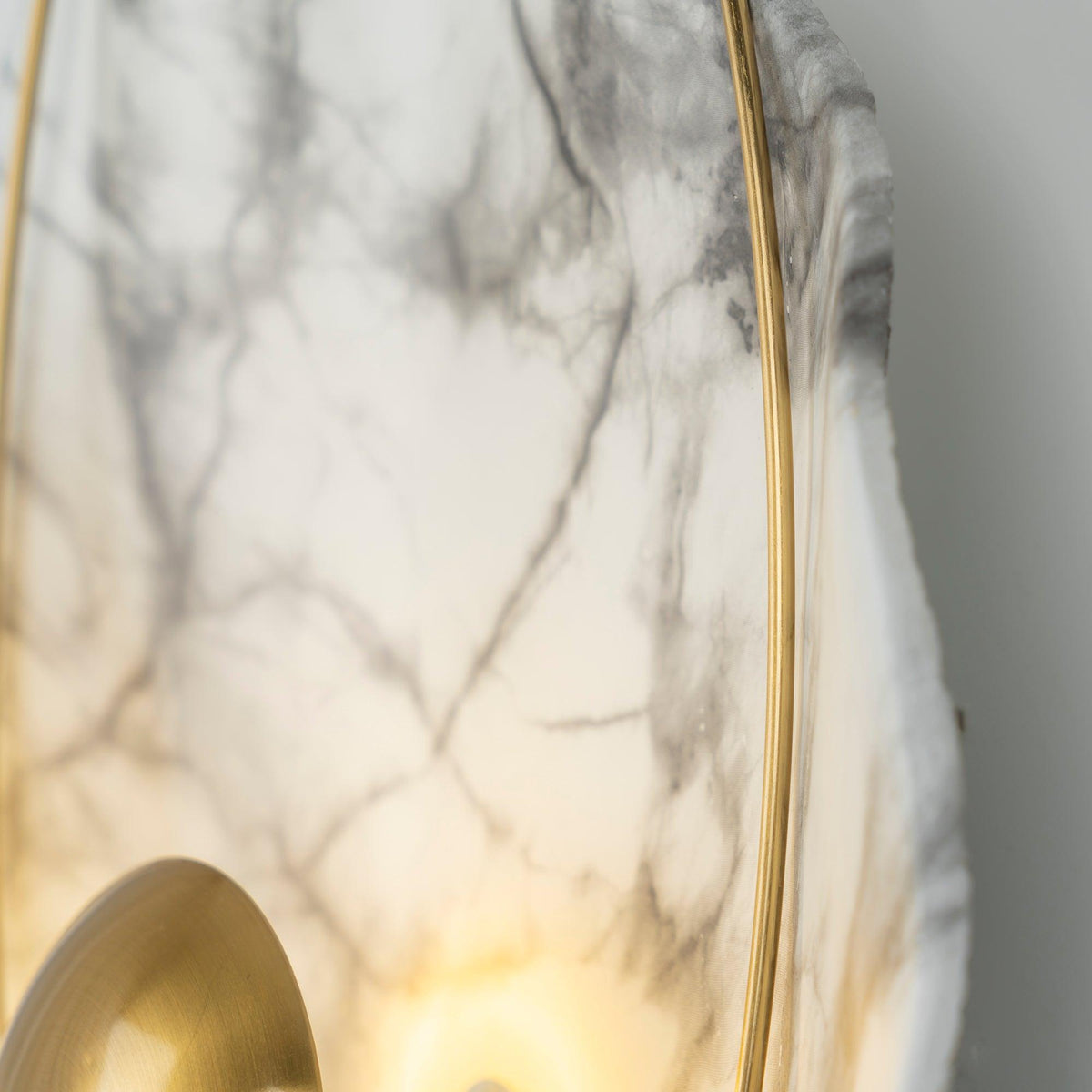 Close crop of grey veining across the marbled face, the brass hoop down one side and the lit orb below.