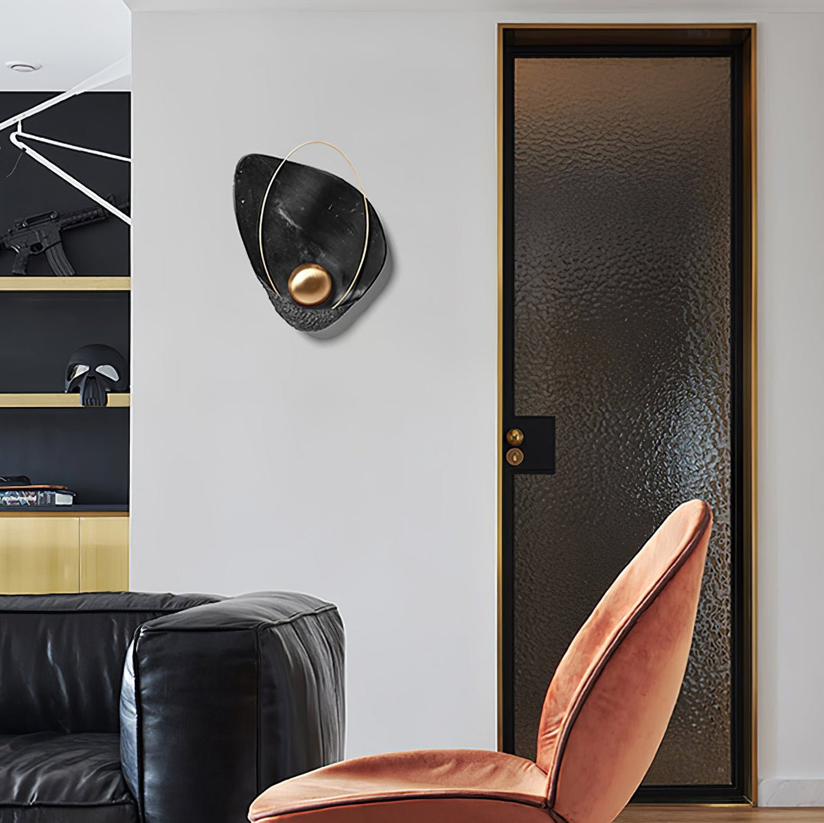 Black marbled sconce unlit on a white wall, beside a dark glass door and a velvet chair.