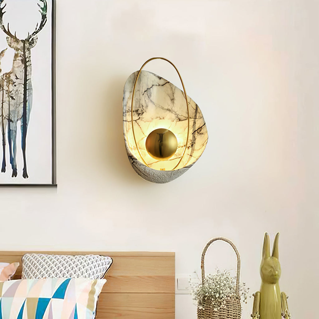 White marbled sconce lit on a cream bedroom wall, with a framed deer print and a bed to its left.