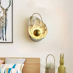 White marbled sconce lit on a cream bedroom wall, with a framed deer print and a bed to its left.