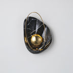 Black marbled sconce lit on a pale grey wall, the brass hoop looping over the top of the shell.