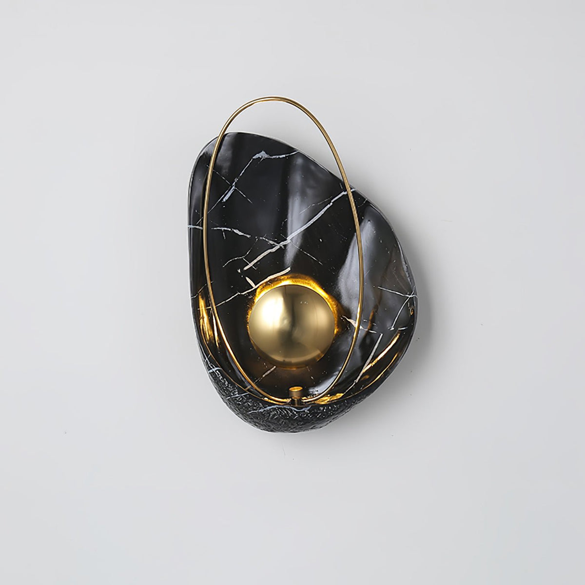 Black marbled sconce lit on a pale grey wall, the brass hoop looping over the top of the shell.