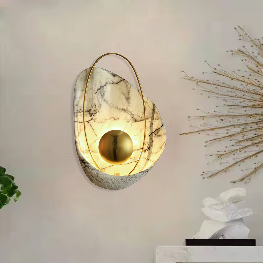 Lit sconce on a pale wall, with a spray of dried branches and a white stone ornament alongside.