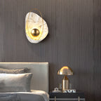 The sconce lit on a fluted dark wood wall above a leather headboard, beside a brass table lamp.