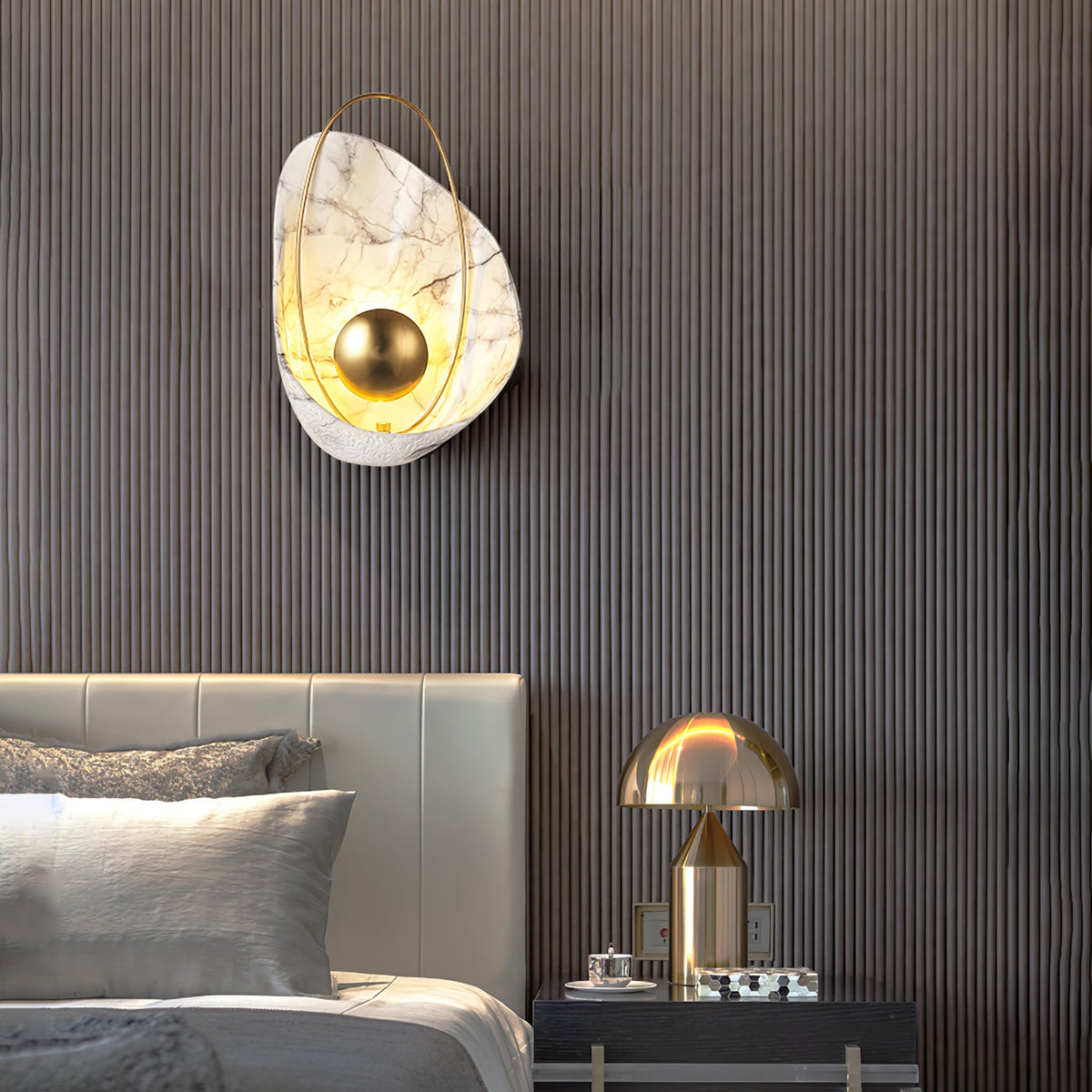 The sconce lit on a fluted dark wood wall above a leather headboard, beside a brass table lamp.