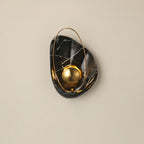 Black marbled sconce lit straight on against a beige wall, white veining across the dark shell.