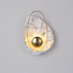 White marbled sconce lit on a pale grey wall, the brass hoop crossing the shell top to base.