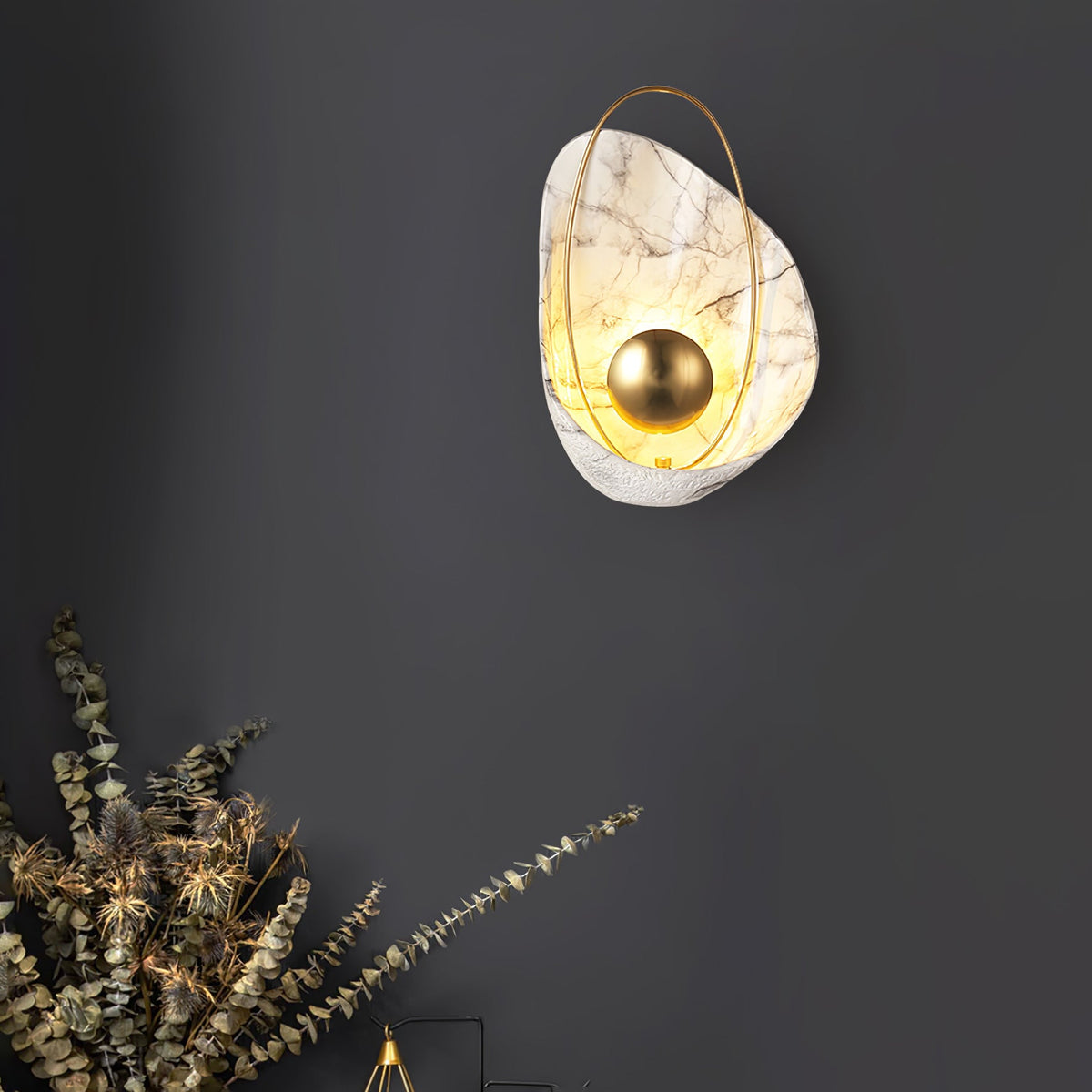 White marbled sconce lit on a charcoal wall, above a spray of dried eucalyptus.