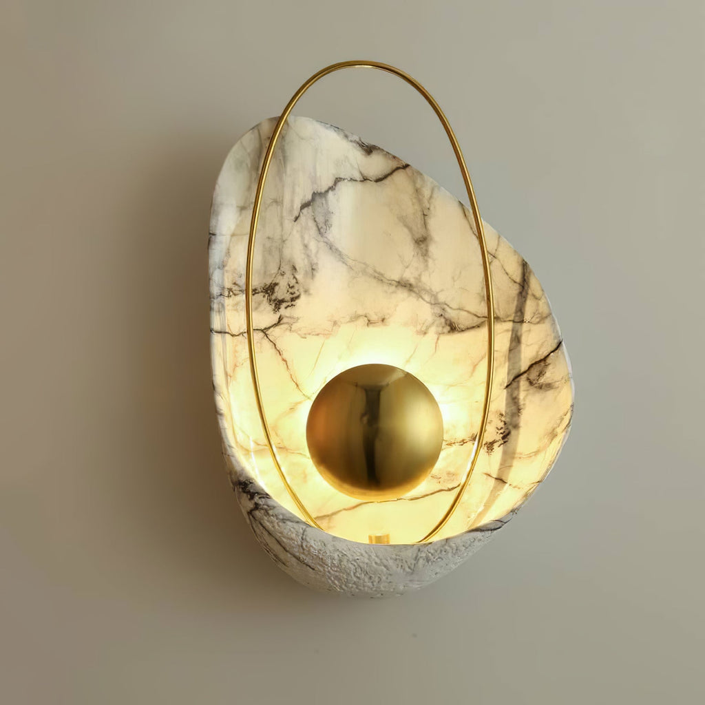 Close angled view of the lit sconce on a warm grey wall, light pooling around the brass orb.