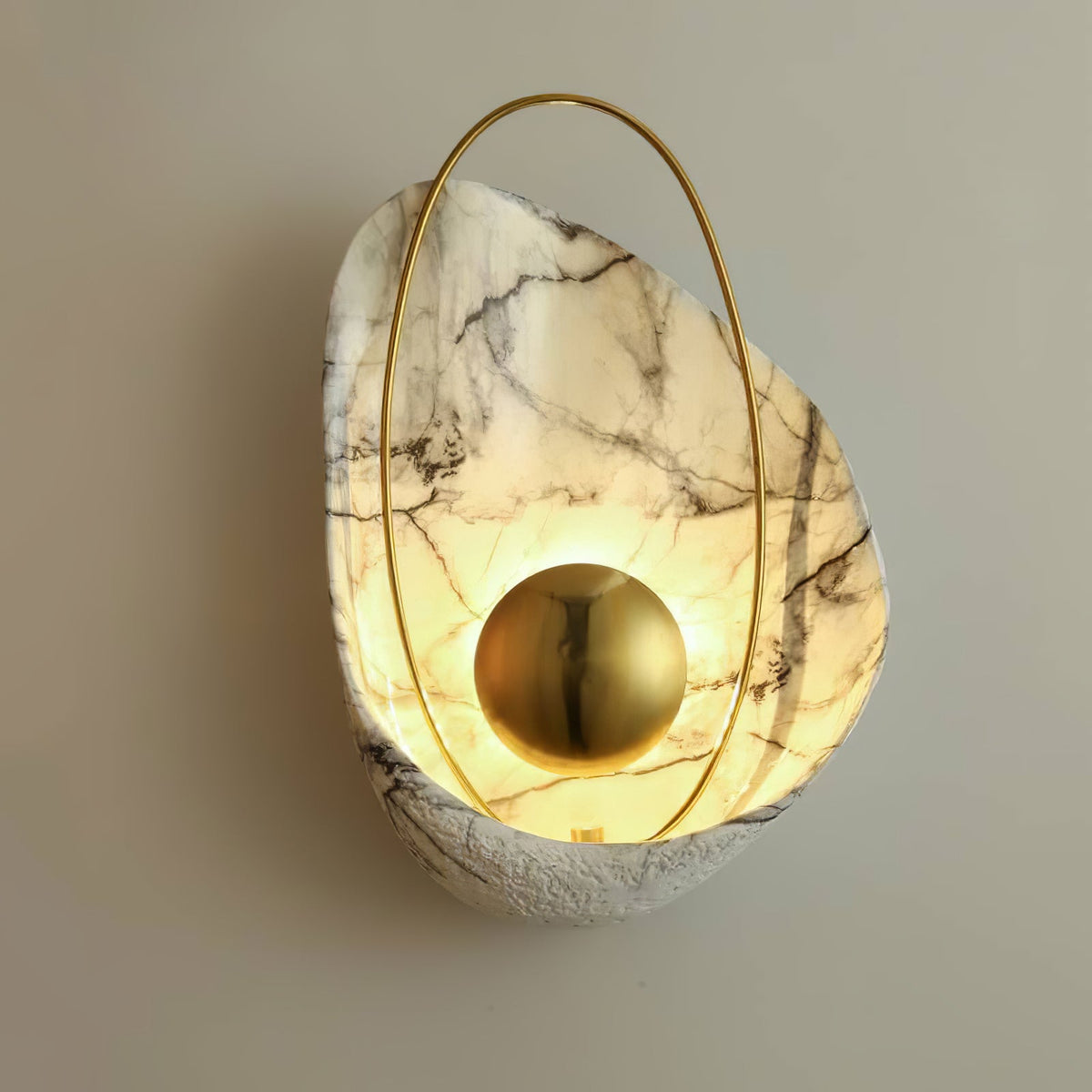 Close angled view of the lit sconce on a warm grey wall, light pooling around the brass orb.