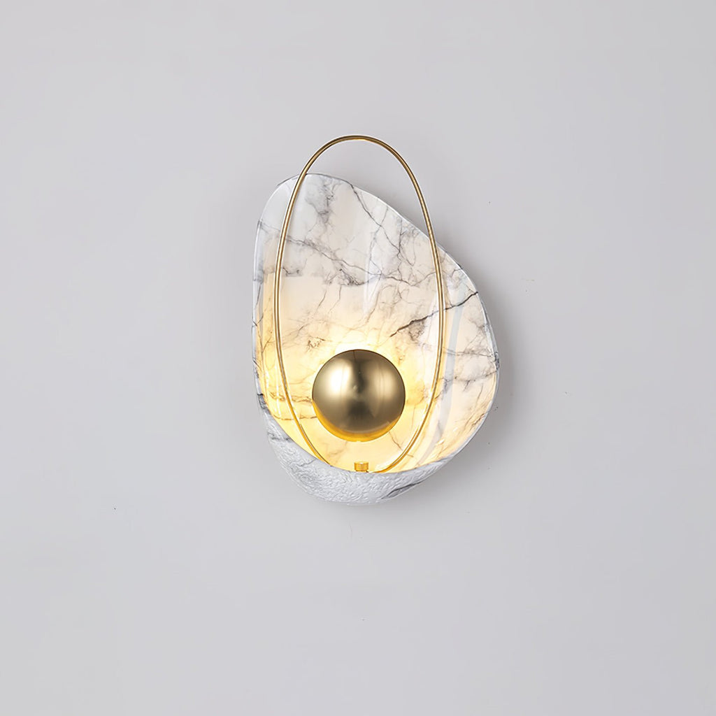 Lit white marbled sconce on a pale grey wall, the warm glow rising through the shell above the orb.