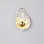 Lit white marbled sconce on a pale grey wall, the warm glow rising through the shell above the orb.