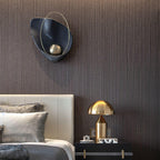 Black marbled sconce with a brass orb, unlit on a fluted dark wall above a leather headboard.