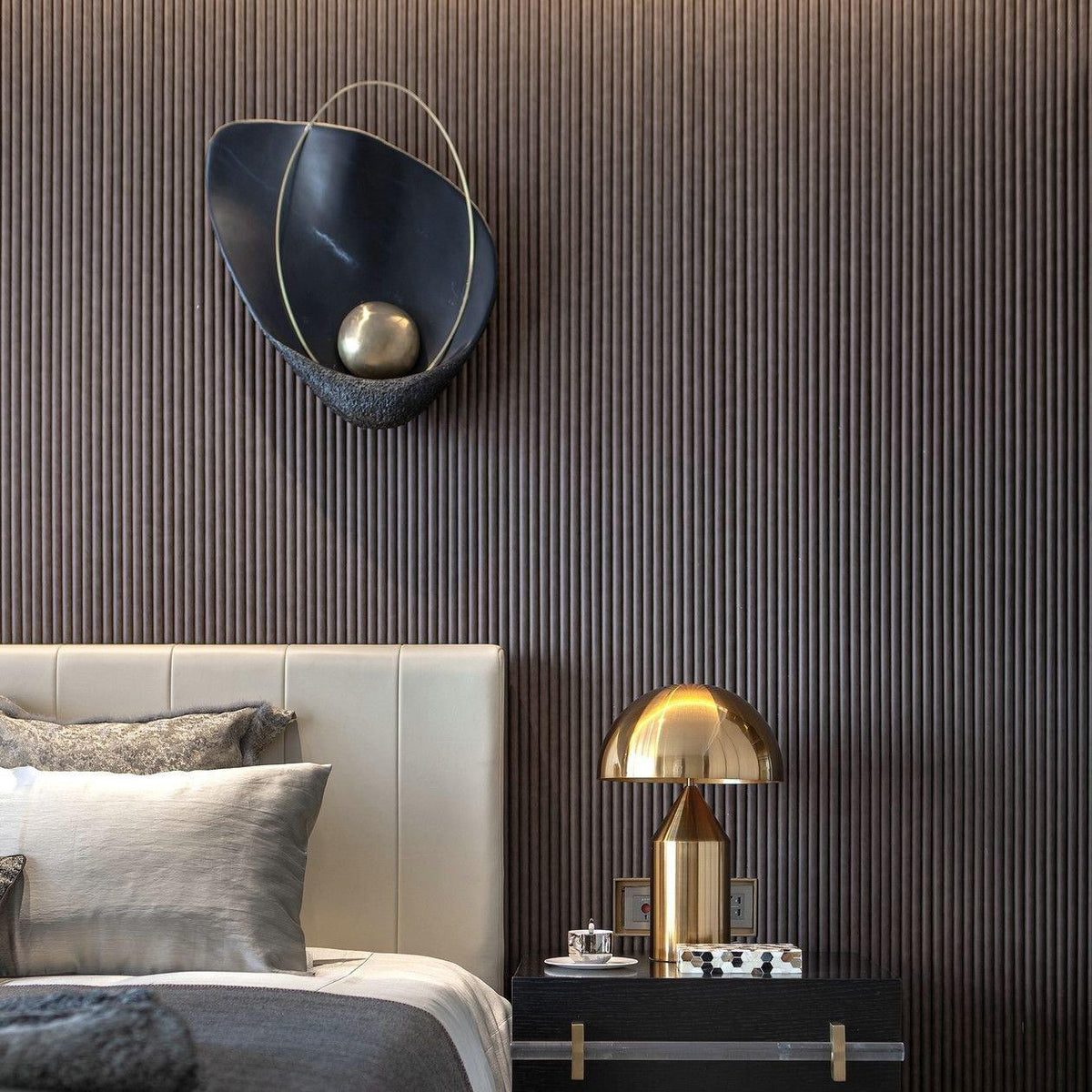 Black marbled sconce with a brass orb, unlit on a fluted dark wall above a leather headboard.