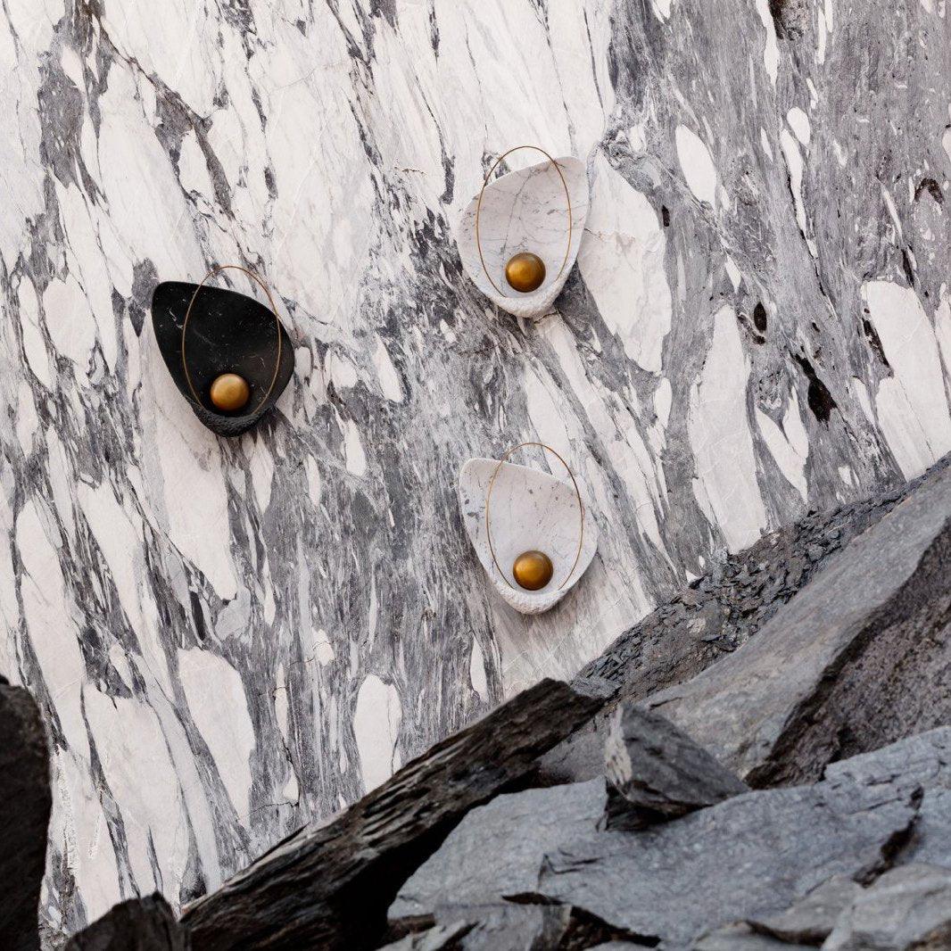 Three sconces, one black and two white, mounted on a veined rock face above slate boulders.