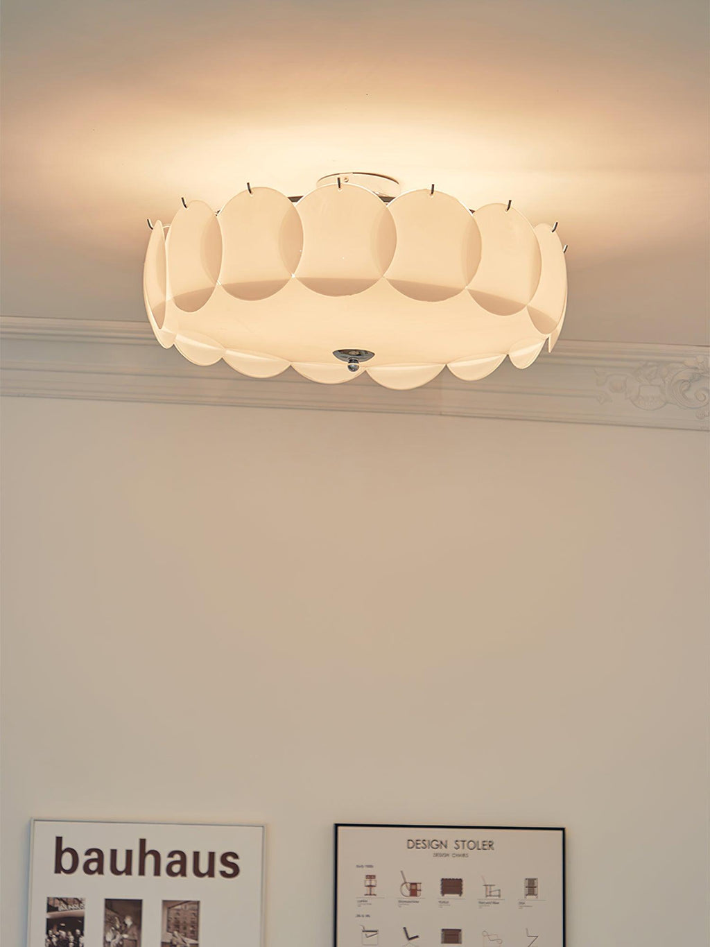 This Clérachic ceiling light glows against a corniced ceiling, with a framed Bauhaus print visible below.