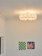 A lit Clérachic ceiling light sits against a corniced ceiling above colourful checkerboard and pop-art prints.