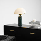 Green marble Veviniel lamp lit on a black dresser beside stacked design books and a bobble candle.