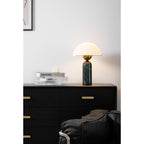 Green marble Veviniel lamp lit on a black sideboard beside a leather chair and design books.