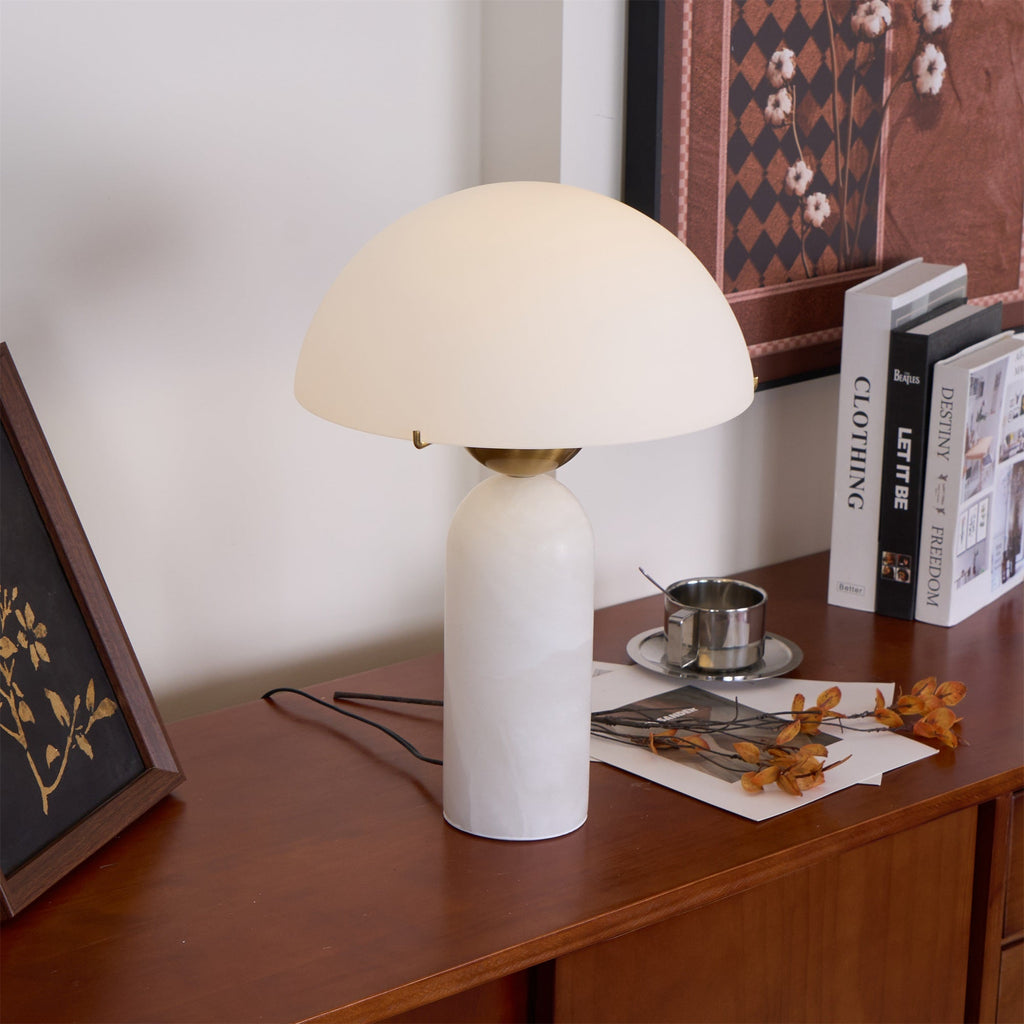 Veviniel lamp angled on a walnut sideboard next to coffee-table books and a small silver cup.