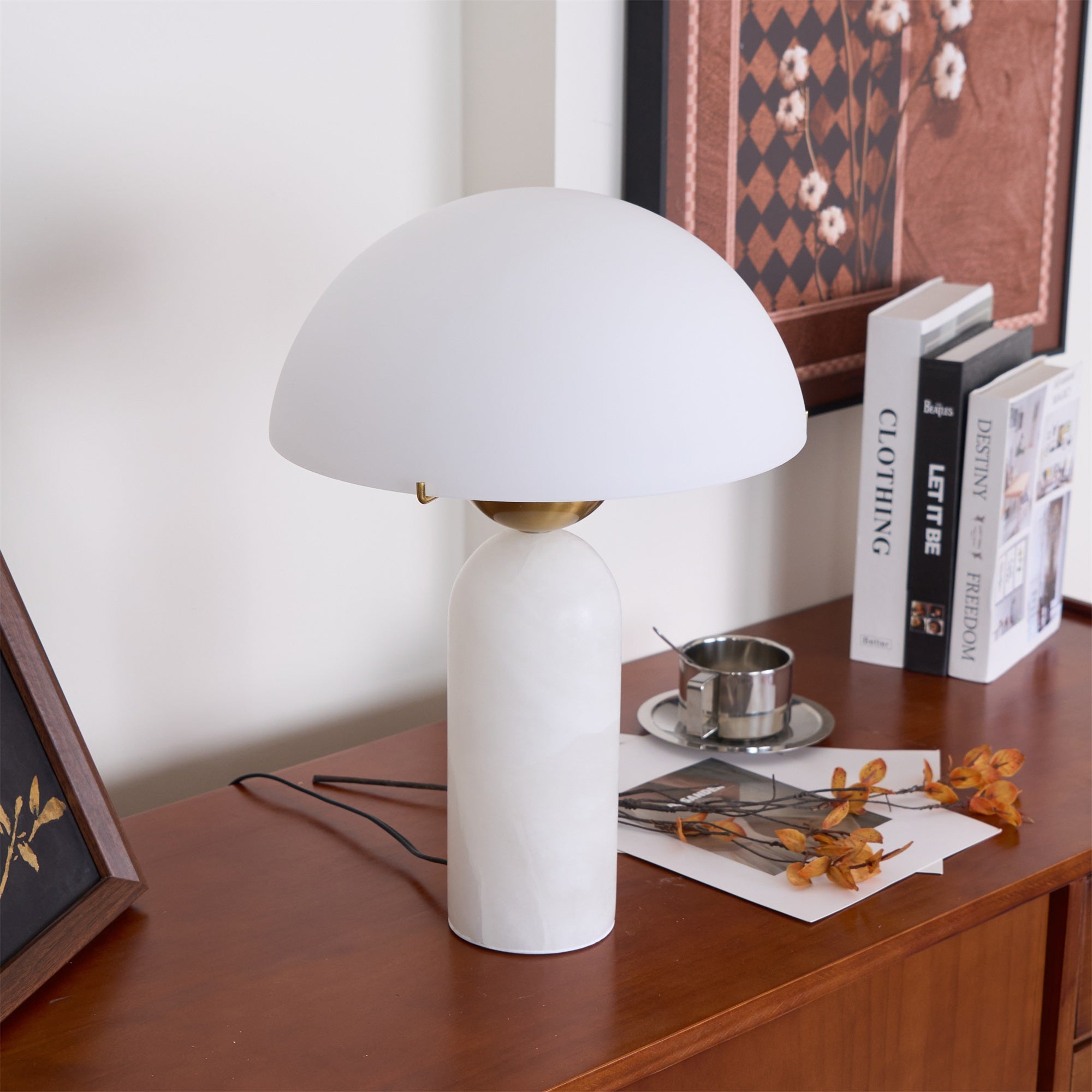 Veviniel lamp with a crisp white shade on a teak sideboard, angled beside books and a silver cup.