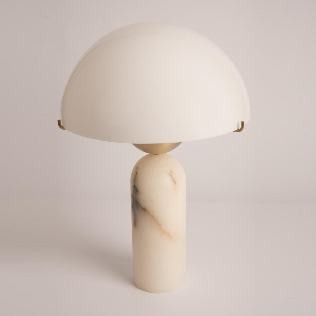 Veviniel alabaster table lamp seen at an angle, its domed shade resting on brass clips above a veined stone column.