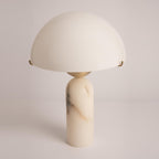 Veviniel alabaster table lamp seen at an angle, its domed shade resting on brass clips above a veined stone column.