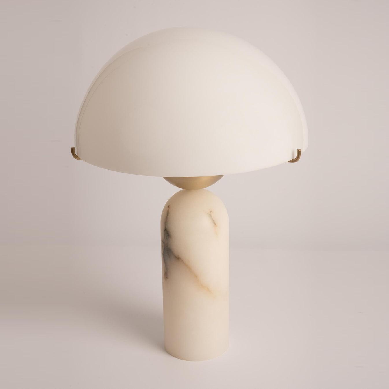 Veviniel alabaster table lamp seen at an angle, its domed shade resting on brass clips above a veined stone column.