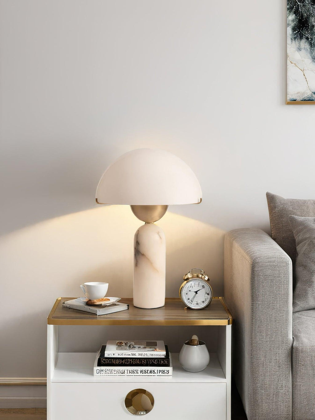 Veviniel lamp lit beside a sofa, warm light spilling onto the wall behind the clock and teacup.