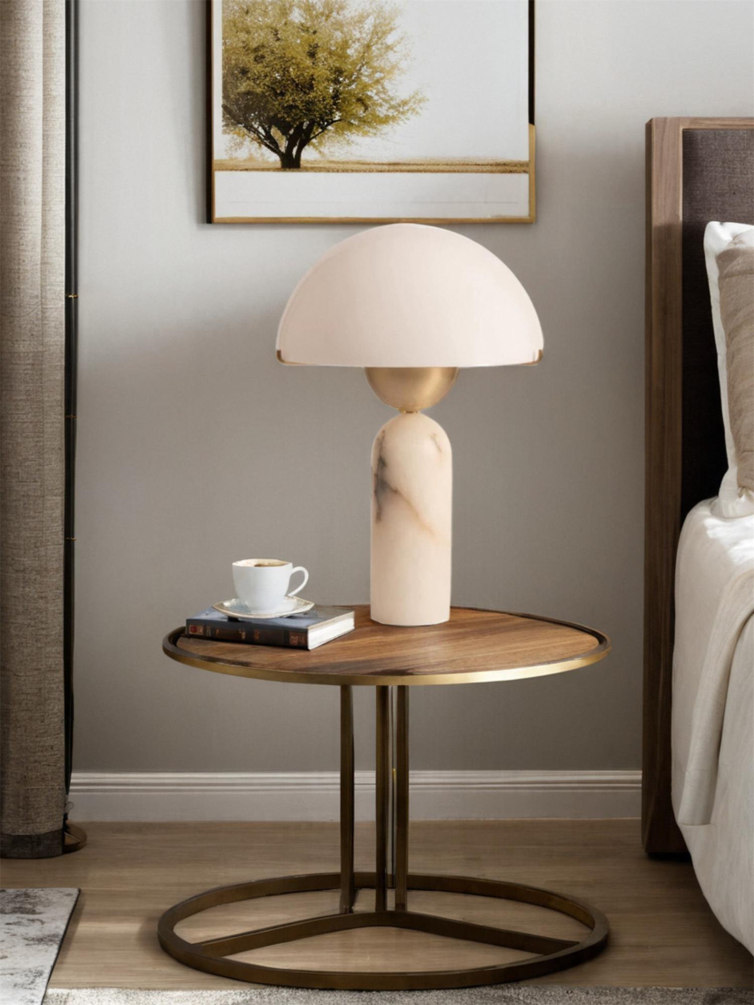 Veviniel lamp on an oval walnut side table beside a bed, with a coffee cup and books alongside.