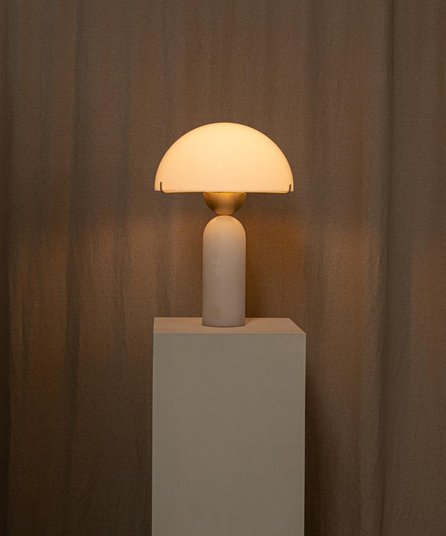 The lamp lit on its plinth, the alabaster shade glowing amber against the linen drape behind.