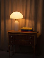 The lit lamp on a wooden chest, its glow reaching across the curtain and the stack of coloured books.