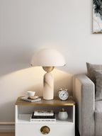 Veviniel lamp lit on a bedside table, throwing a warm arc of light up the wall beside a grey sofa.
