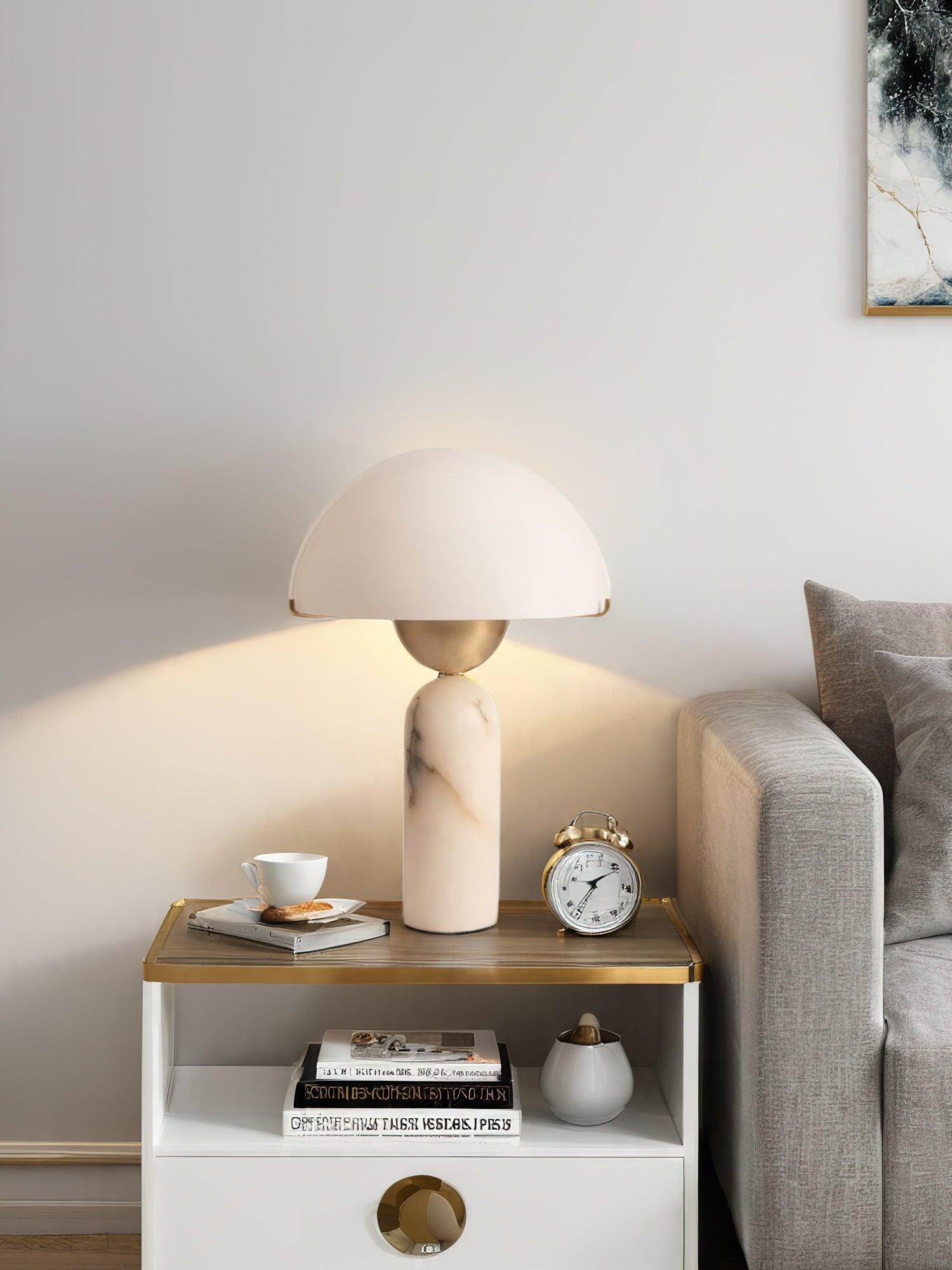 Veviniel lamp lit on a bedside table, throwing a warm arc of light up the wall beside a grey sofa.