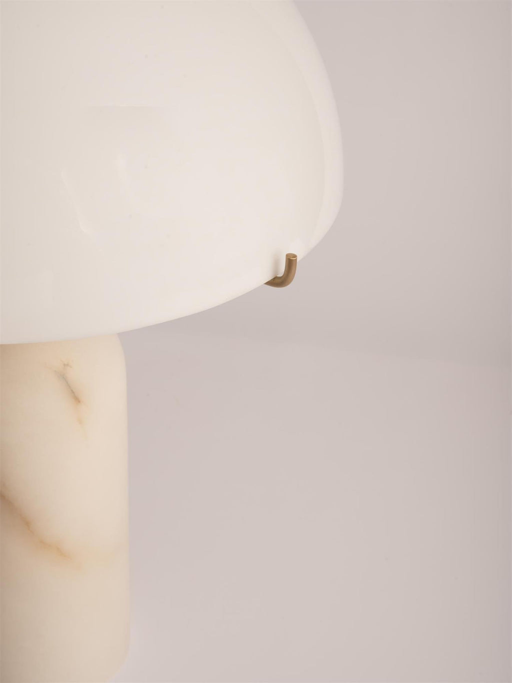 Close-up of the brass hook clip holding the shade edge, with the veining of the alabaster column below.