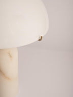 Close-up of the brass hook clip holding the shade edge, with the veining of the alabaster column below.