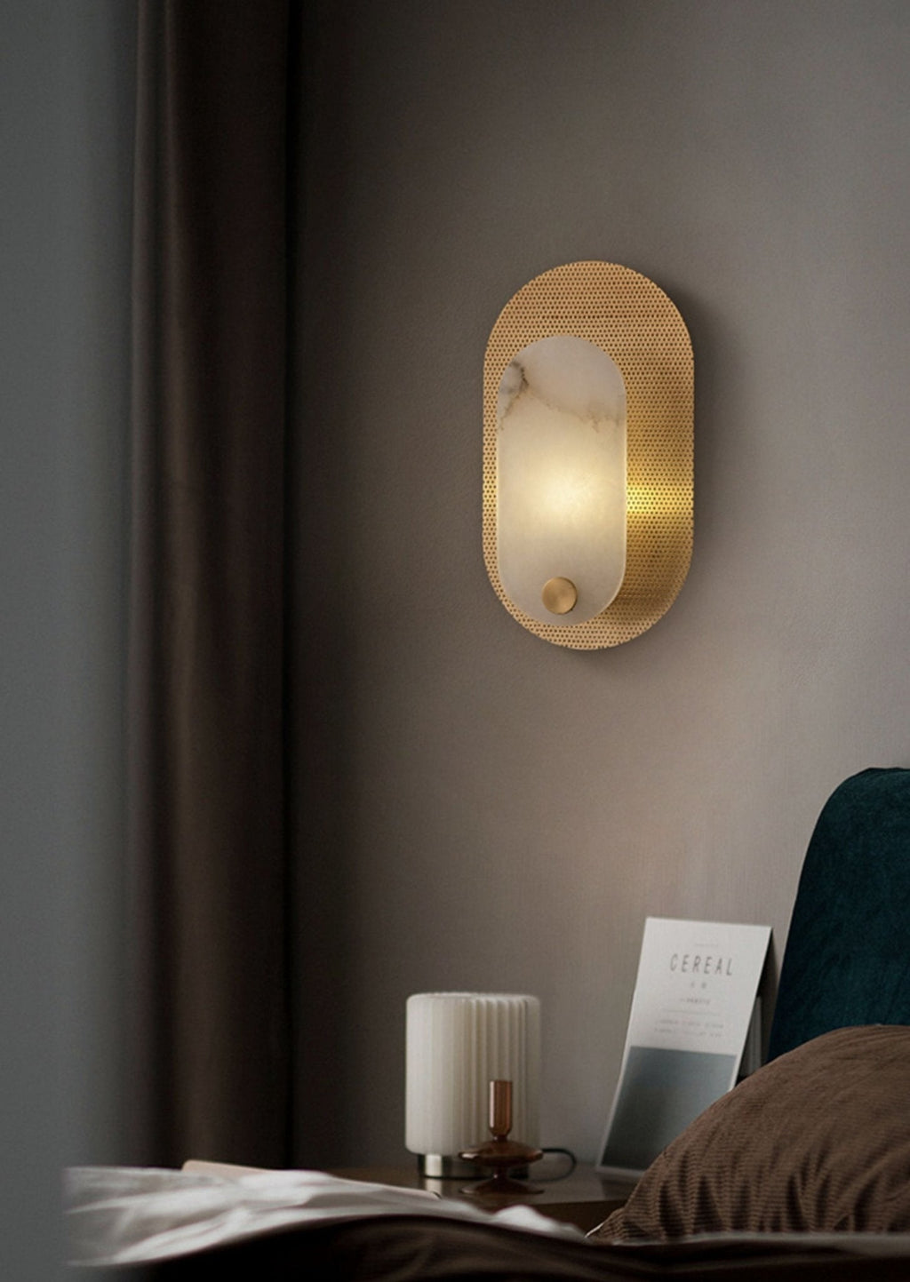 The sconce lit in a bedroom beside a curtain, with a ribbed lamp and magazine on the nightstand.
