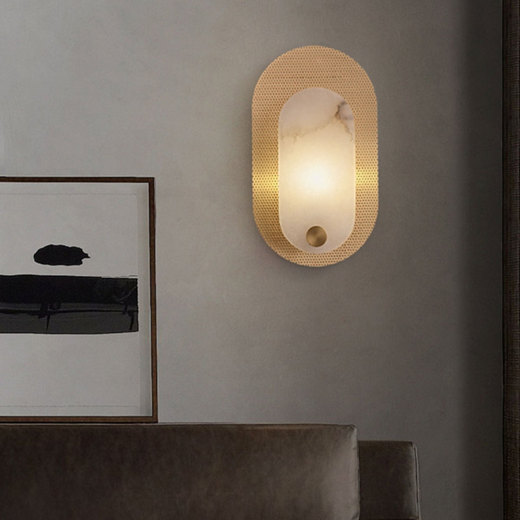 The sconce lit on a grey wall beside a framed abstract print, above a dark leather sofa.