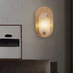 The sconce lit on a grey wall beside a framed abstract print, above a dark leather sofa.