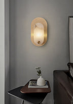 Lit on a grey wall above a black side table holding a white vase of small flowers.