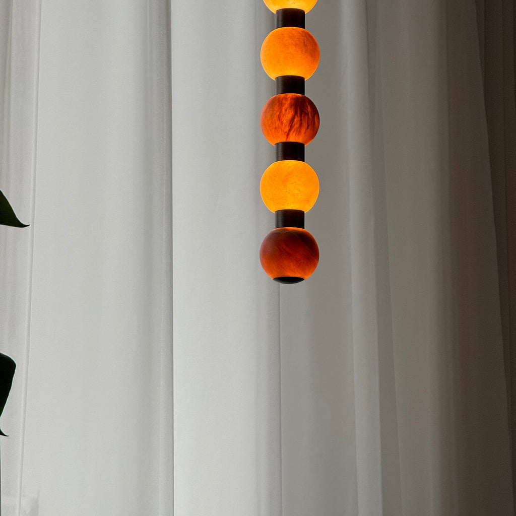 The upper spheres of this Clérachic pendant glow warm amber against a softly lit curtain.