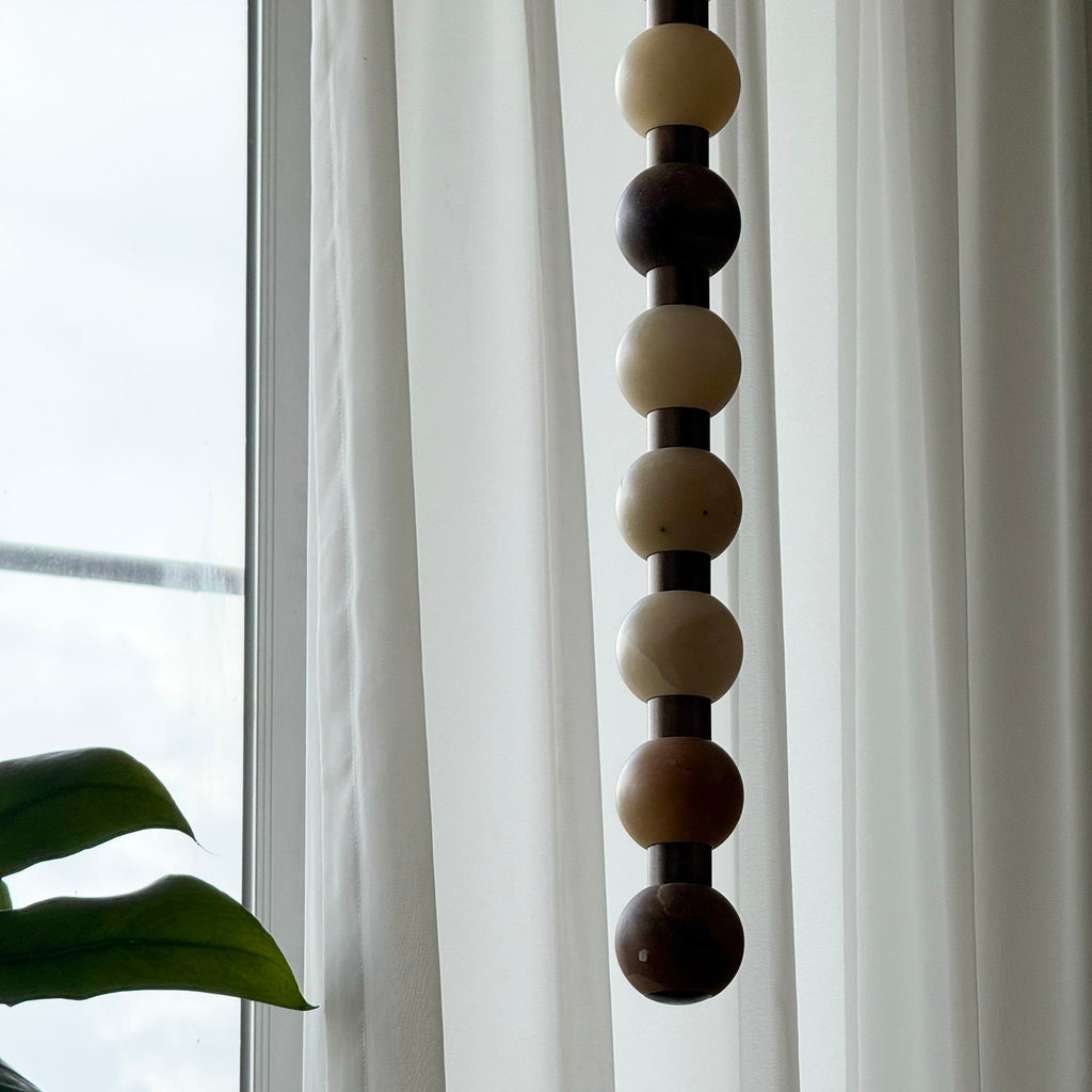 The upper spheres of this Clérachic pendant show pale cream and dark brown stone against a curtain.