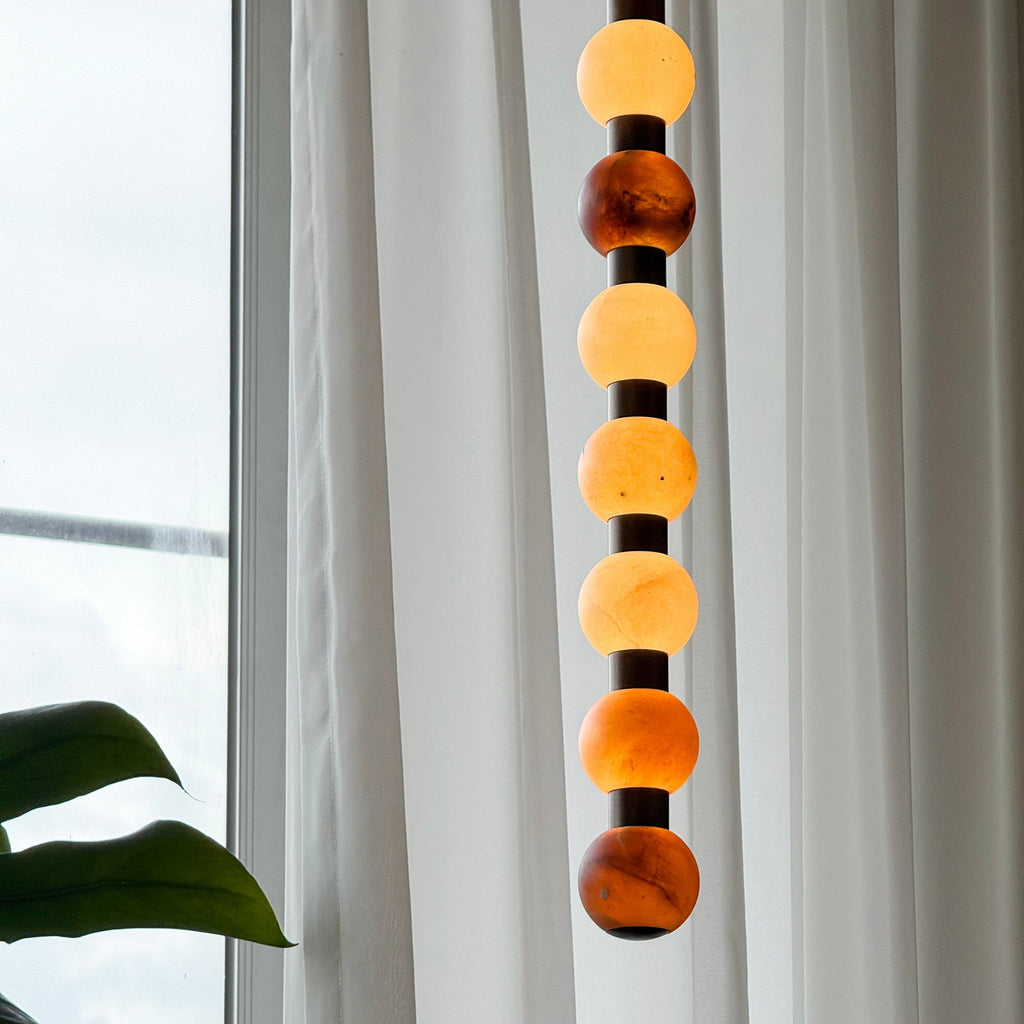 Warm light glows through the varied stone tones of this Clérachic pendant against a sheer curtain.