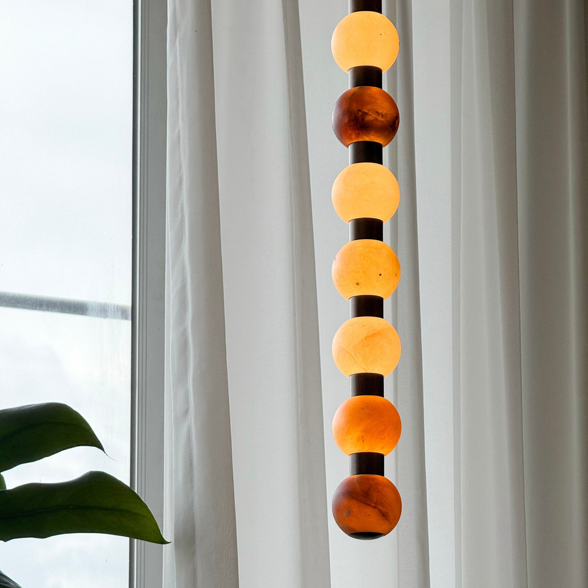 Warm light glows through the varied stone tones of this Clérachic pendant against a sheer curtain.