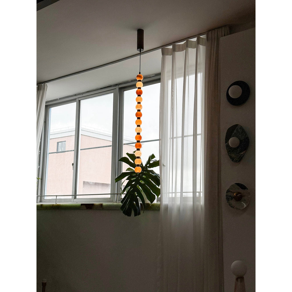 The full drop of this Clérachic pendant hangs beside a window, a monstera leaf below and wall discs above.